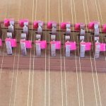 Detail image of harpsichord action. Strings are oriented vertical in the image with a row of jacks with red felt.