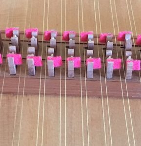 Detail image of harpsichord action. Strings are oriented vertical in the image with a row of jacks with red felt.
