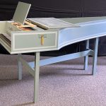 Image of a single manual harpsichord. It is a pale green color with white accents and a yellow tassel.