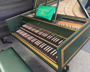 Image of a green harpsichord with open lid and music stand. The case and lid are accented with gold boxes